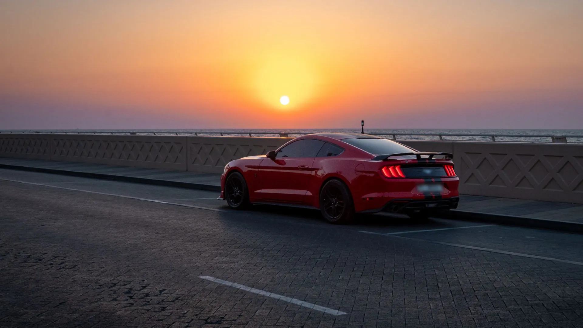 Carro esportivo vermelho estacionado na orla diante do pôr do sol