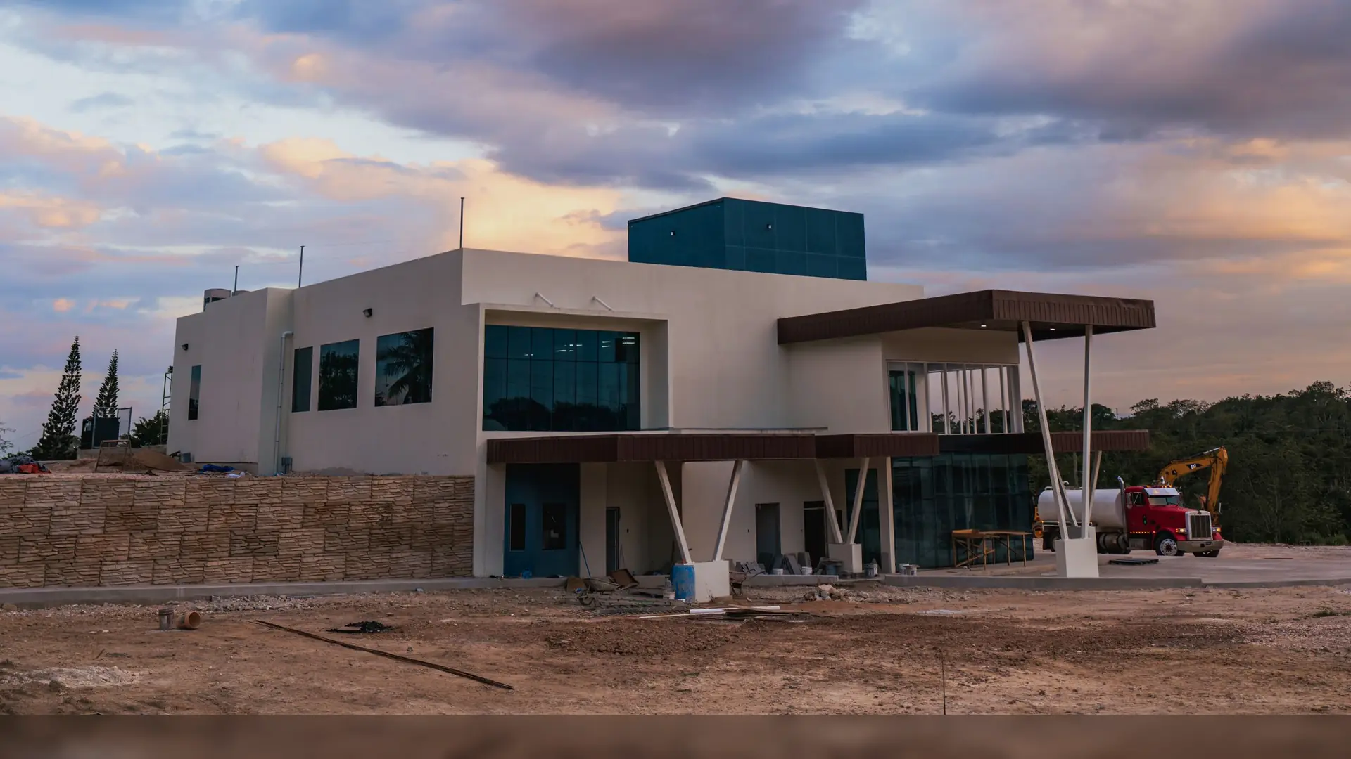 Casa contemporânea em fase final de obra, com o terreno ainda em terra, sob o céu do entardecer